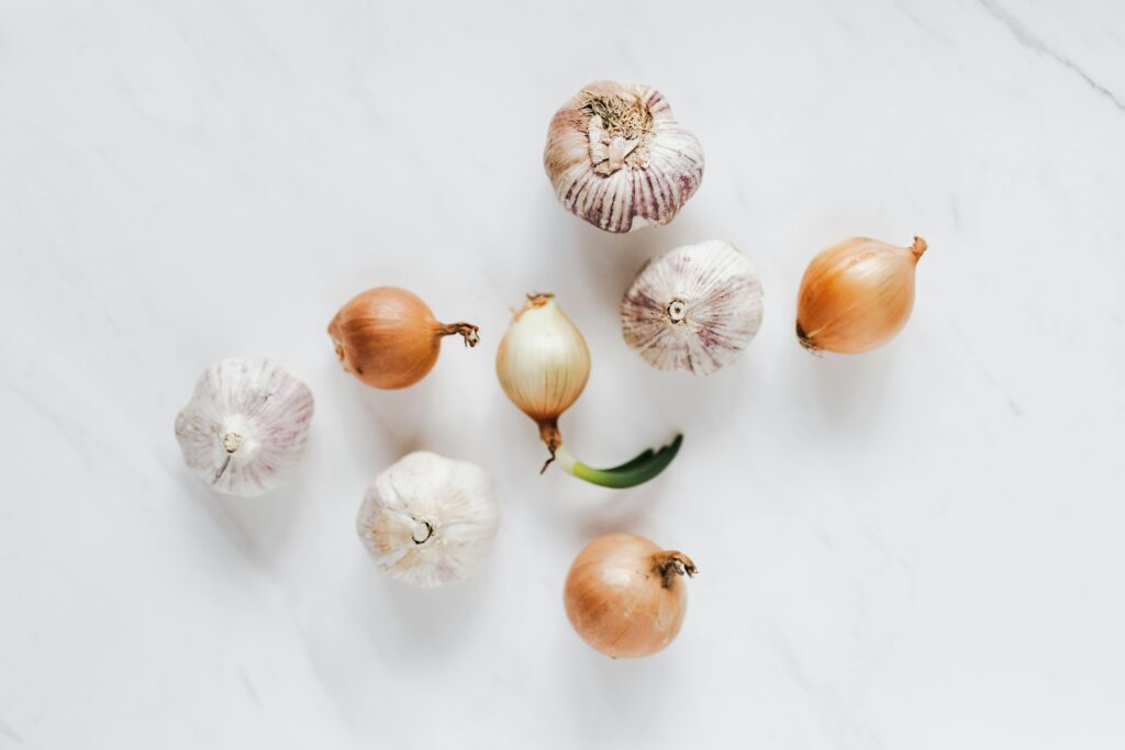 Garlic bulbs and onions on a white surface used for making homemade organic pest control sprays—affordable, chemical-free options for container garden pest prevention.