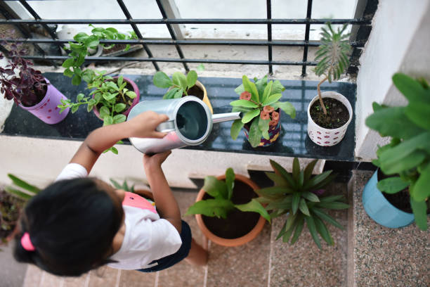 Child watering indoor potted plants on a balcony, showing simple seasonal care routine for container gardening and winter watering tips to keep plants healthy.