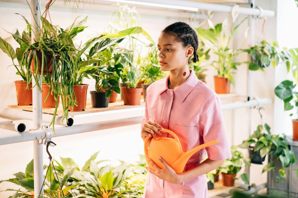Beginner watering indoor potted plants using a watering can in an organized container gardening setup, showing a simple routine for consistent plant care in a small space